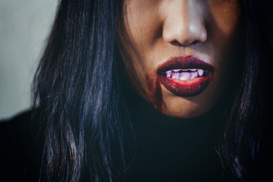 Close up Red lips scary with blood and fangs halloween concept, Mysterious demon girl with red lips. Vampire Witch lady with blood in mouth on black background.