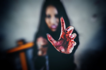 Bloody hands of a young woman witch protruding forward with fangs and black background