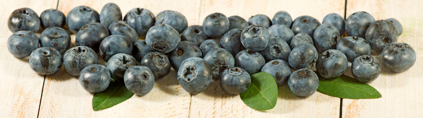 Group of blueberry berries with leaves on a wooden surface closeup.