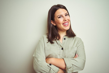 Young beautiful brunette woman wearing green shirt over isolated background happy face smiling with crossed arms looking at the camera. Positive person.