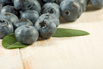 Group of blueberry berries with leaves on a wooden surface closeup.