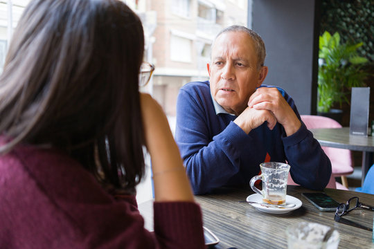Senior man having a conversation with woman drinking coffee and relaxing, chatting at restaurant