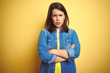 Young beautiful brunette woman wearing casual denim jacket over yellow isolated background skeptic...