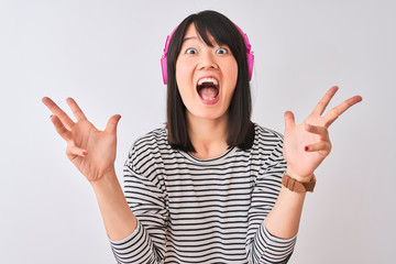 Chinese woman listening to music using pink headphones over isolated white background celebrating crazy and amazed for success with arms raised and open eyes screaming excited. Winner concept