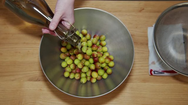 A Japanese female chef pouring Shochu (Japanese distilled spirit) over Japanese Ume (making UMEBOSHI) at home kitchen, Tokyo, Japan. May 2019. Camera fixed, Extreme close-up, bird's eye view