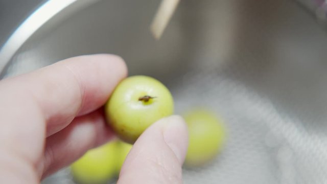 A Japanese female chef removing stem of Japanese Ume to make UMEBOSHI at home kitchen, Tokyo, Japan. May 2019. Camera fixed, Extreme close-up, high angle