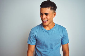 Young brazilian man wearing blue t-shirt standing over isolated white background winking looking at the camera with sexy expression, cheerful and happy face.