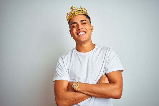 Young Brazilian Man Wearing King Crown Standing Over Isolated White Background Happy Face Smiling With Crossed Arms Looking At The Camera. Positive Person.