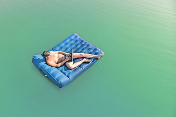 Man with the laptop on an air mattress in water, top view