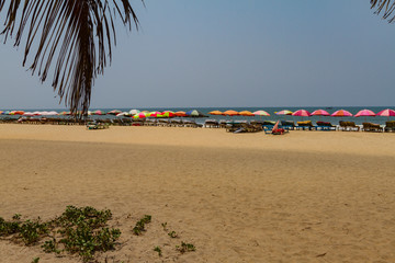 Wooden deck chairs with colorful parasols on the beach in GOA, India. Sea summer holiday template.