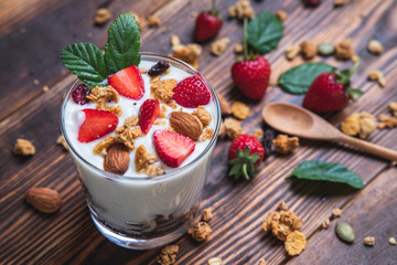 Top view bowl of homemade granola and yogurt mixed with fresh strawberries on a wooden table along with almonds on the side.