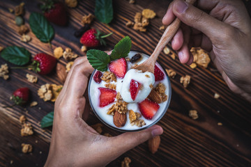 Health concept - Top view hands holding a spoon, yogurt and strawberry on a wooden table.