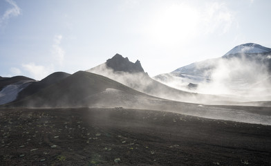 Misty magical morning in Avacha base camp. Kamchatka Peninsula, Russian far east. Mountain peaks and ribs of the volcano. Clouds creating mystical landscape. Direct sun through veil of fog