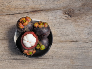 Top view a group delicious ripe Purple Mangosteens in black bowl on wood texture blurred background.