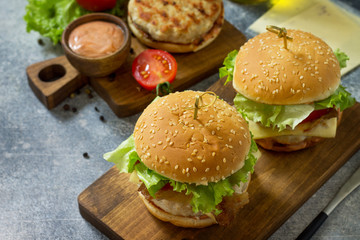 Two homemade burgers with cutlet of chicken meat, melted cheese, tomatoes and bacon on a wooden board.
