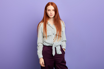 confident cheerful ginger girl in fashion stylish striped blouse and pants with hand on his pocket looking at camera.clothes and fashion , close up portrait, isolated blue background, studio shot
