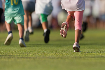 Running children, young athletes run in a kids run race, running on grass detail on legs, running in the light of morning