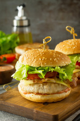 Delicious grilled burgers, hamburger sandwich with cutlet of chicken meat, melted cheese, tomatoes and bacon on a wooden board.Free space for your text.