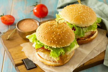 Two homemade burgers with cutlet of chicken meat, melted cheese, tomatoes and bacon on a wooden board.