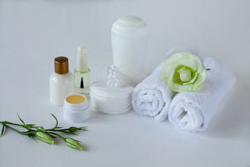 Close up of the set for body care: a few rolled towels, antiperspirant, cotton pads, cotton buds, bottle of lotion, balsam for lips, nail polish with eustoma on the white background