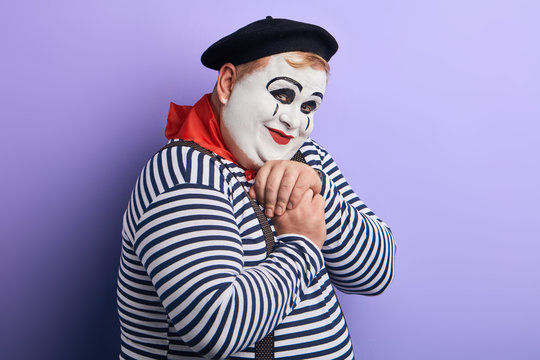 Portrait of a shy and flirty fat mime giving admiring look. Man falls in love, holding hands clasped and feeling awkward. Romantic comedy concept.isolated blue background, studio shot