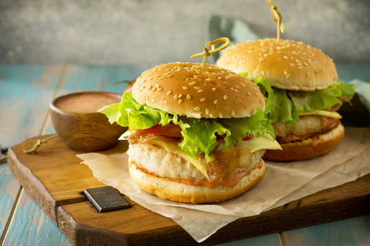 Two Homemade Burgers With Cutlet Of Chicken Meat, Melted Cheese, Tomatoes And Bacon On A Wooden Board. Free Space For Your Text.