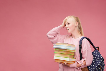 portrait of a beautiful girl student with a backpack and a stack of books in his hands is smiling at the pink background.