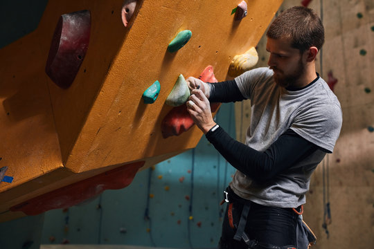 Side view of young physically challenged boulderer fixing artificial rocks and holds at climbing wall, preparing to intensive training, professional sport hobby, active lifestyle concept.