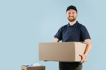 Cheerful delivery man in uniform is holding big cardboard box