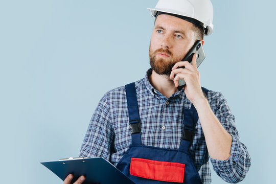 Conserned construction worker in a white helmet and blue overalls with a phone