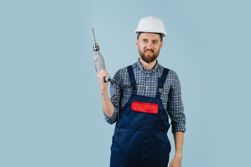 Happy construction worker in a white helmet and blue overalls with a hand drill