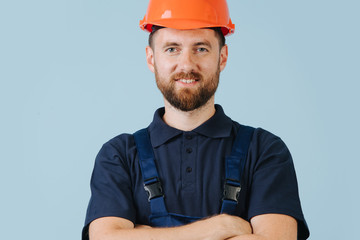 Confident construction worker in a orange helmet and blue uniform, hands crossed