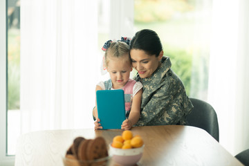 Obraz na płótnie Canvas Daughter sitting near mom in military uniform and watching cartoon