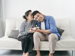 Happy Asian man giving gift box to his mother for Mother's Day celebration.