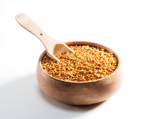 Fenugreek (Trigonella) in a wooden cup with a scoop on a white background