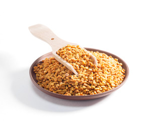 Fenugreek (Trigonetla) on a clay plate with a wooden scoop on a white background