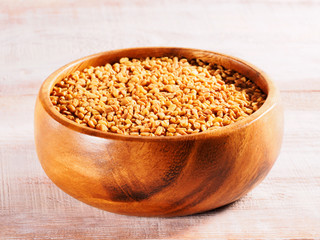 Fenugreek (Trigonella) in a wooden cup on a wooden background