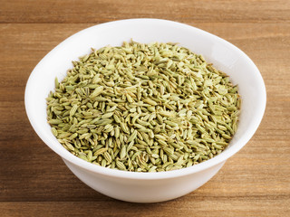 Fennel seeds (Foeniculum vulgare) in a white cup with scoop on a wooden background
