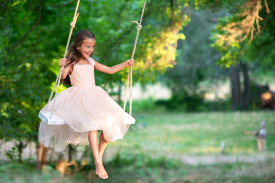 Happy girl rides on a swing in park. Little Princess has fun outdoor, summer nature outdoor.