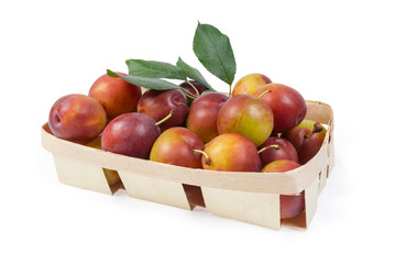Fresh plums with leaves in wooden basket on white background