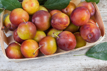 Top view of fragment of wooden basket with plums, closeup
