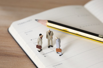 Miniature businessman standing on a calendar with a pen next to them having a business meeting and discussing strategys