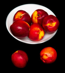 Ripe nectarine in a white plate on a black background
