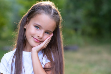 Pretty little girl with long brown hair posing summer nature outdoor. Kid's portrait. Beautiful child's face