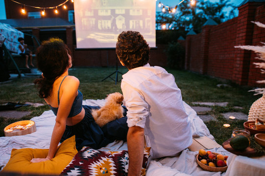 Couple In Love Watching A Movie, In Twilight, Outside On The Lawn In A Courtyard