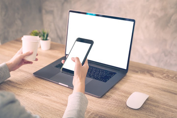 Hipster women holding phone and using laptop on wooden table in coffee shop.