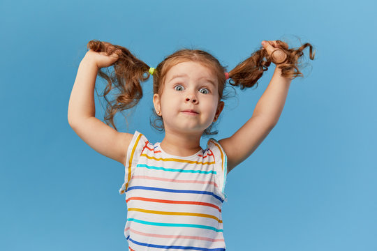 Naklejki Portrait of surprised smiling cute little toddler girl. child standing isolated over blue background. Looking at camera and laughs