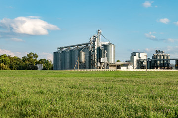 Fototapeta na wymiar silver silos on agro manufacturing plant for processing drying cleaning and storage of agricultural products, flour, cereals and grain with beautiful clouds