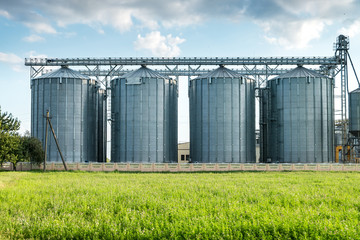 silver silos on agro manufacturing plant for processing drying cleaning and storage of agricultural products, flour, cereals and grain with beautiful clouds