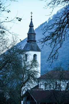 The bell tower of an old church in winter. Dark surroundings and woods in the background. Travel in Europe, Slovenia, Tolmin. Forest on a mountain in the background.